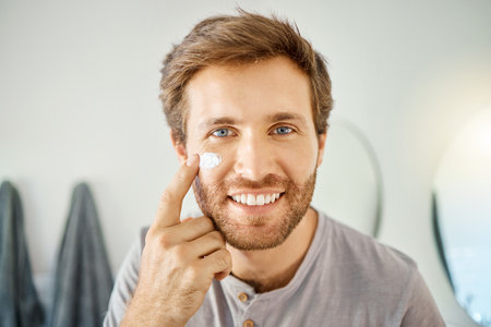Bathroom, portrait and happy man with skincare cream for acne treatment, skin hydration or home beauty routine. Face cosmetics, dermatology smile or hygiene person with morning sunscreen applicationの写真素材