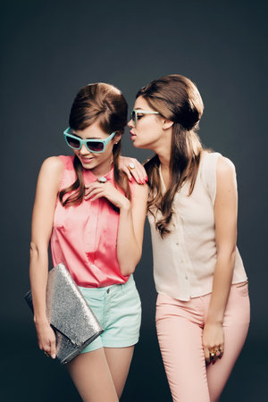 Fashion, vintage and secret with women and whisper in studio for elegant, pastel and beauty. Sunglasses, confident and cosmetics with female model on dark background for glamour, beehive and styleの写真素材