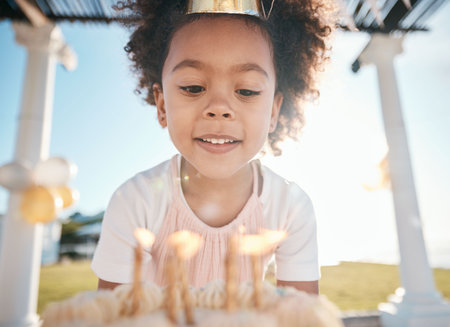 Cake, girl and candles for birthday party in garden for fun with balloons or hat with snack. Excited, kid and dessert to make a wish for celebration in summer at house for child with milestone.の写真素材