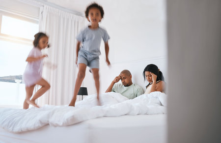 Young kids, jump and parents on bed with playing, game and excited in family house in morning. Naughty sibling children, mother and father in bedroom with bond, love and childhood development in homeの写真素材