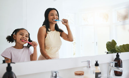 Brushing teeth, hygiene and a mother with her daughter in the bathroom of their home together for a morning routine. Kids, dental and toothbrush with a woman parent teaching her child about oral careの写真素材