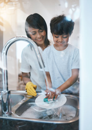 Woman, boy child and dishes at kitchen sink for learning, cleaning and hygiene with care in family house. Mother, boy and washing play with soap, water and teaching for skills, chore or stop bacteriaの写真素材