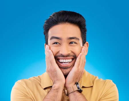 Happy, excited man and surprise face in studio with Asian model with teeth and joy. Blue background, male person and casual fashion with handsome and friendly guy with modern style and wow smileの写真素材
