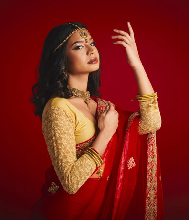 Portrait, confident and Indian woman with fashion, traditional dress and beauty against a red studio...