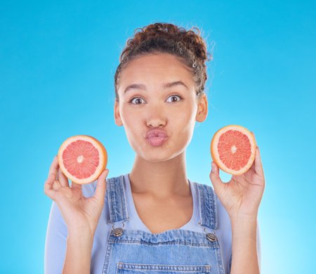 Portrait, kiss and woman with grapefruit in studio isolated on a blue background. Face, fruit and person with food for healthy diet, nutrition or wellness, eating and vitamin c, benefits and vegan.の写真素材