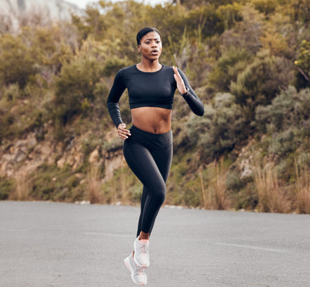Mountain, running and woman for fitness, exercise and speed training, outdoor challenge and focus on road. Fast professional runner, athlete or african sports person for cardio workout or marathonの写真素材