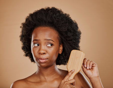 Sad black woman, hair and unhappy with brush in studio, brown background and afro. Beauty, worried african female model and comb hairstyle with anxiety, knot and problem of damage to natural textureの写真素材