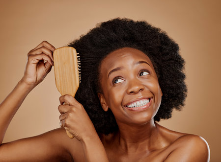 Black woman, hairstyle and smile for brush in studio, brown background and treatment for curly texture. Natural beauty, confidence and happy young african female model comb clean or healthy afro hairの写真素材
