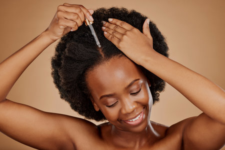 Oil serum, hair care or black woman with afro in studio on brown background for a healthy scalp. Smile, pipette or natural African girl at hairdresser salon for hairstyle treatment or beauty makeoverの写真素材