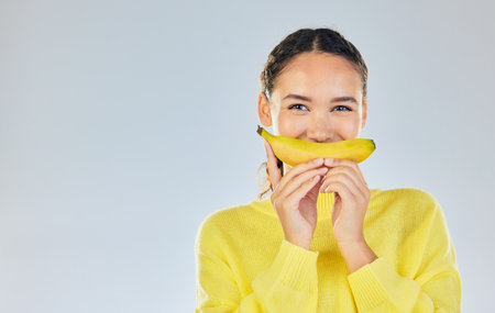 Happy, banana and portrait of woman with fruit in studio for healthy eating, wellness and diet. Food, lose weight and mockup person on white background with fruits for nutrition, detox and digestionの写真素材