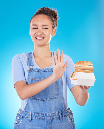 Burger, no and woman reject fast food choice and unhappy gives bad, disgust and frustrated review for diet protection. Disaster, mistake and person disappointed isolated in a studio blue backgroundの写真素材