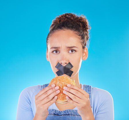 Burger, diet and woman reject fast food choice and unhappy gives bad, disgust and frustrated review for protection. Disaster, mistake and person disappointed isolated in a studio blue backgroundの写真素材