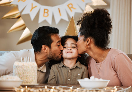 Father, mother and child at birthday party, kiss and happy with celebration, care and bonding in family house. Dad, mom and young kid with event, excited face and love together at table in apartmentの写真素材