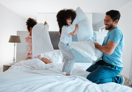 Happy family, pillow fight and playing on bed in the morning together for fun bonding at home. Father, mother and playful children enjoying game, entertainment or fighting with pillows in the bedroomの写真素材