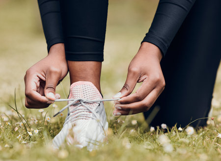 Lace sneakers, person and hands outdoor on grass for running, workout and performance. Closeup of athlete, runner and tie shoes on feet, footwear and exercise at park for sports, fitness and marathonの写真素材