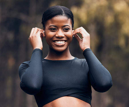 Fitness, black woman listening to music and in forest with earphones happy for motivation. Training or workout, exercise or health wellness and female athlete listen to radio or podcast in woodsの写真素材