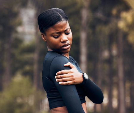 Shoulder, pain and sports woman outdoor for health risk, bruise and hands on wound in park. Fitness, black female athlete and arm injury of muscle, joint problem and first aid for exercise accidentの写真素材