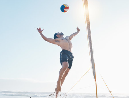 Beach, exercise and man with fitness, volleyball and fun with sunshine, moving and healthy. Male person, athlete and player with seaside sports, game with speed or workout goals with sand or wellnessの写真素材