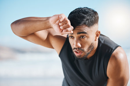 Tired, sweating and fitness break for man outdoor after training, running or cardio workout on blurred background. Sweat, face and Indian male runner with sports fatigue, dehydration from exerciseの写真素材
