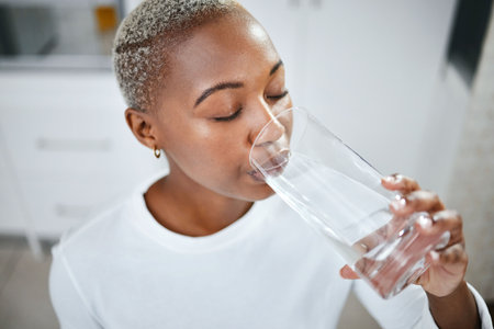 Health, glass and woman drinking water for hydration, wellness and liquid nutrition at her home. Thirsty, energy and African female person enjoying cold healthy drink in the kitchen of her apartment.の写真素材