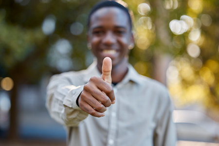 Black man, hands and thumbs up in park for good job, approval or success in the nature outdoors. Portrait of happy African male person show thumb emoji, yes sign or like for agreement or deal outsideの写真素材