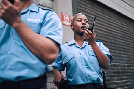 Security, walkie talkie and a black woman police officer in the city during her patrol for safety or law enforcement. Radio, communication and service with a female guard on a street in an urban townの写真素材