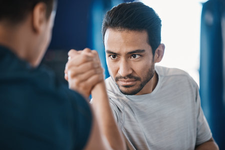Arm wrestling, men and strength challenge with strong muscle at a gym for battle. Hand wrestle,...
