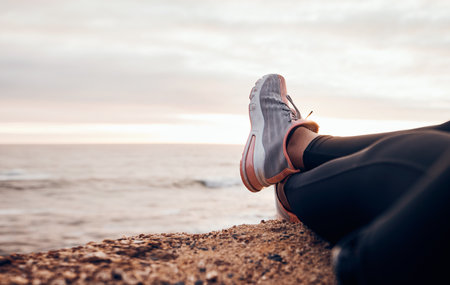 Fitness, shoes and sea in nature relax with freedom outdoor sitting. Waves, ocean and water with a person and athlete taking a break from training and workout with feet in sunset with mockup spaceの写真素材