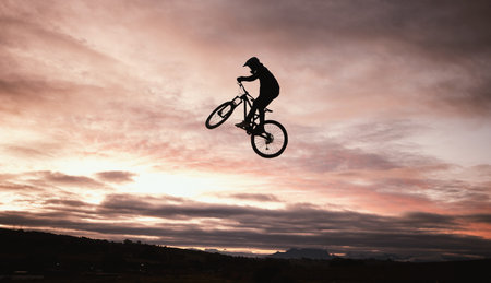 Sunset, dirt bike and jump with action in outdoor with sport in nature for adventure or risk. Motorcycle, silhouette and freedom with training or sky with speed in desert with person driving.の写真素材