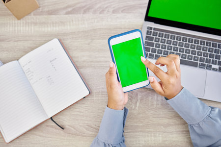 Technology, hands of woman with smartphone and green screen on laptop with notebook for research. Planning or mockup space, online communication or internet and top view of female person at officeの写真素材