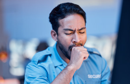 Security officer, man and tired at work with uniform or late night working for career in protection. Exhausted, safety professional and guard with yawn or guy during shift at desk with burnout.の写真素材