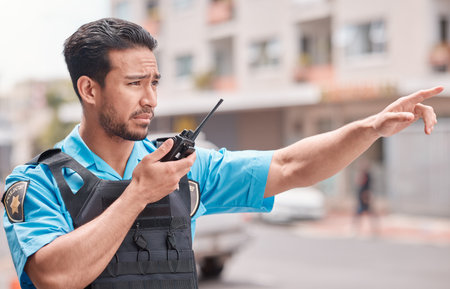 Asian man, police and pointing with walkie talkie in city for emergency dispatch, arrest or calling suspect. Male person, cop or law enforcement with radio signal for communication or safety in townの写真素材