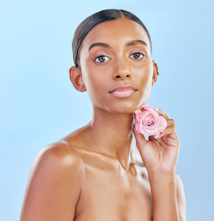 Woman, rose and natural beauty with cosmetics and eco friendly skincare on blue background. Flower, nature and sustainable dermatology with skin glow, female model and portrait in studioの写真素材