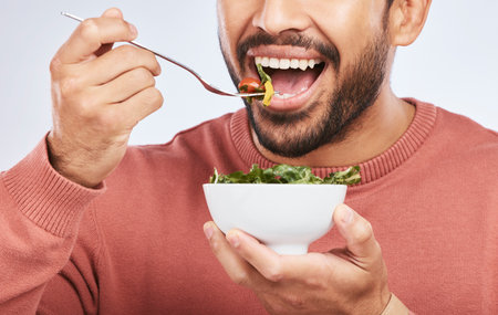 Health studio, man and mouth eating salad, vegetables or green food product for weight loss, healthy lifestyle or nutrition. Closeup nutritionist, lettuce bowl and hungry person on white backgroundの写真素材