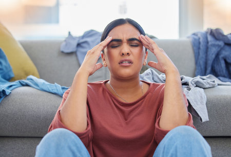 Headache, stress and woman with depression from laundry in a living room, exhausted and unhappy in her home. Anxiety, migraine and female person frustrated with household, task or spring cleaningの写真素材
