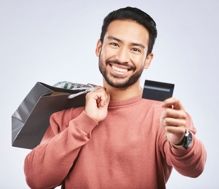 Shopping bag, portrait or man with smile, debit card and happiness for retail fashion spree, sales discount or boutique deal. Promotion face, studio credit payment or happy person on white backgroundの写真素材