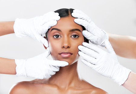 Woman, plastic surgery and hands in studio portrait with beauty, skincare and face with process by white background. Change, model and doctors gloves for transformation, cosmetics or facial aestheticの写真素材