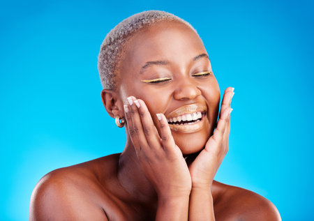 Face makeup, smile and happy black woman with facial application, aesthetic cosmetics and skincare hydration glow. Beauty eyeliner, collagen shine and African studio person on blue background.の写真素材