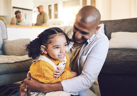 Happy family, smile and father with girl child on living room floor playing, laugh and bond in their home together. Love, hug and kid with parent in a lounge for tickle, fun and games on the weekendの写真素材