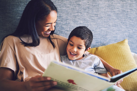 Family home, mother and child reading a book in a bed together with love, care and security or comfort. Woman and kid with a happy smile and quality time for learning or story in bedroom to relaxの写真素材