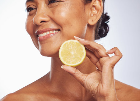 Thinking, orange and senior woman with skincare, cosmetics and vitamin c against a white studio background. Mature female person, happy lady or model with citrus fruit, natural beauty and nutritionの写真素材