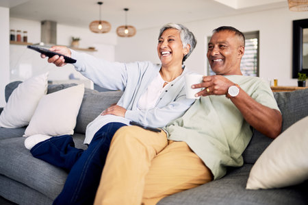 Senior couple, watching tv and relax on sofa in home living room, laughing and together for funny comedy show. Elderly man, old woman and happy for streaming comic movie on lounge couch in houseの写真素材