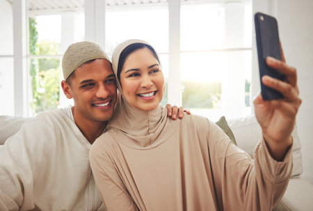 Selfie, Islam and happy couple on couch with smile, culture and love in living room in Indonesia. Marriage, man and woman in hijab on sofa together with respect, religion and photo for social media.の写真素材