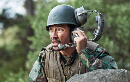 Army, battle and a man with a headset for communication in a field, help or call for danger. Veteran, hero and a person in the military with gear for support, talking or advice in nature for safetyの写真素材