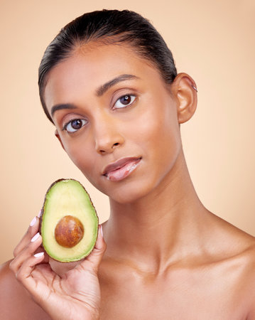 Avocado, skincare and woman in portrait for healthy face and natural beauty on studio brown background. Young indian person or model with green fruits, vitamin c benefits and dermatology or cosmeticsの写真素材