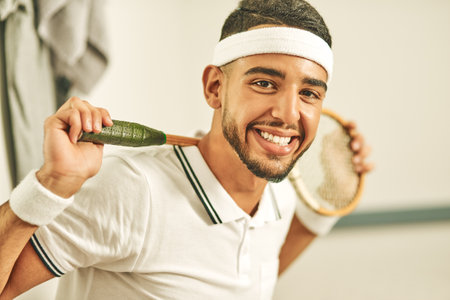 Squash is my passion. Portrait of a happy young man holding his squash racket in the locker room.の写真素材