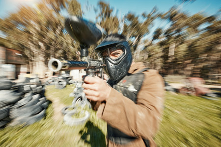 Paintball, shooting and gaming with man in playground for battlefield, mission or soldier with blur. Sports, games and fast with person and gun in arena for challenge, adventure and warrior trainingの写真素材