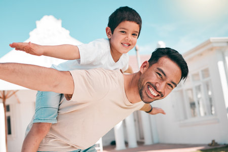 Happy, airplane and portrait of a father with his child in the outdoor garden at their family home. Playful, smile and young dad carrying his boy kid on his back while bonding and playing together.の写真素材