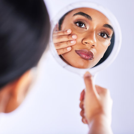 Studio, skincare and portrait of woman with mirror for skin, check or facial results on grey background. Beauty, reflection and female model with cosmetic, inspection and dermatology wellness routineの写真素材