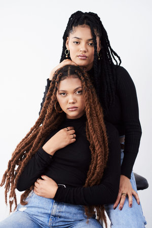 Long natural hair is what they love. Studio shot of two beautiful young women posing against a grey...